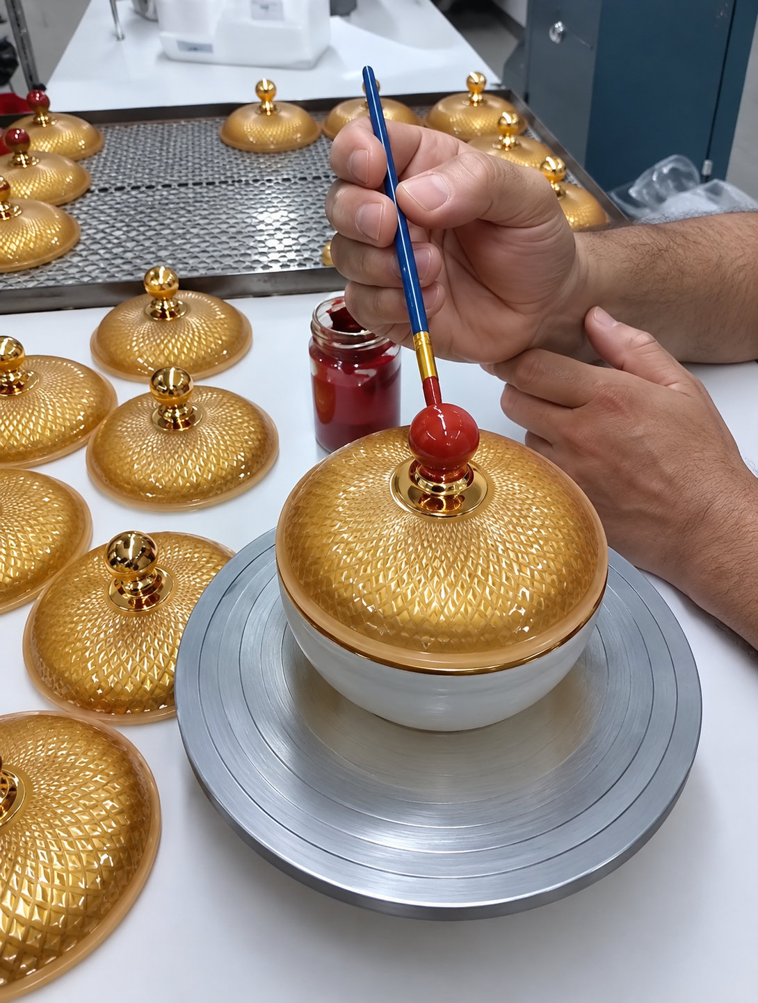 Hand painting a red detail on a gold-decorated lid